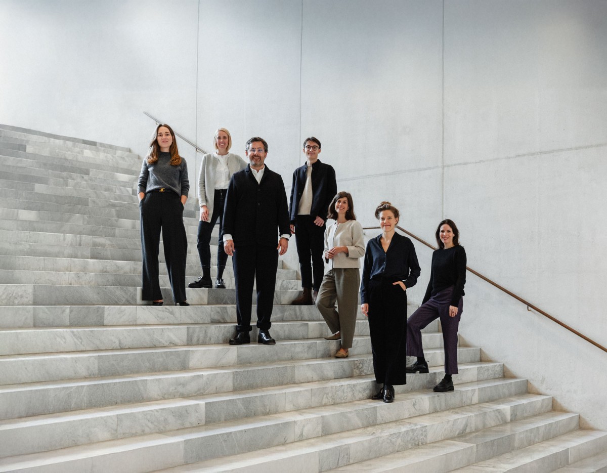 Das FUTUN-Kollektiv steht auf Treppenstufen in einem Treppenhaus aus Marmor und Beton