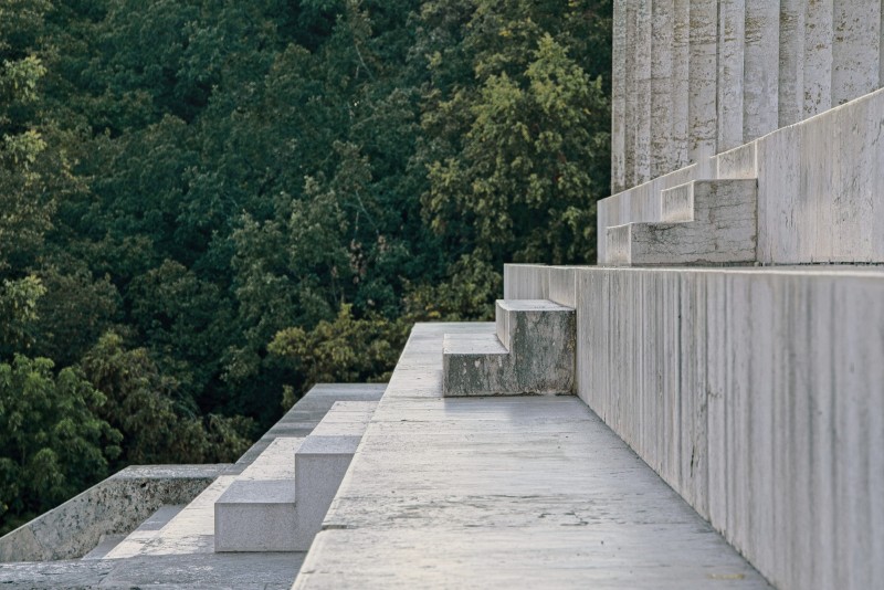 Eine Marmortreppe geht aufsteigend von links nach rechts durchs Bild, im Hintergrund ein dichter Wald